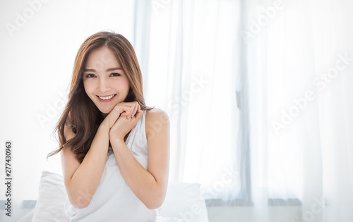 Portrait of beautiful young sexy asian woman with attractive smile enjoy fresh bedding linen mattress in white bed room apartment. Teenage girl sleep resting, good night sleep facial skincare concept.