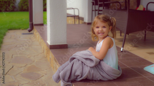 Baby sitting near the house have fun. Girl smiling looking at the camera sits on the stairs at the backyard. Happy caucasian child enjoy summer season outdoors.
