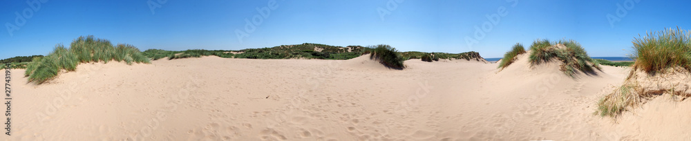 a long panoramic view of the grass covered coastal sand dunes in front of the sea in formby merseyside on a bright summer day with blue sky