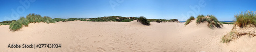 a long panoramic view of the grass covered coastal sand dunes in front of the sea in formby merseyside on a bright summer day with blue sky