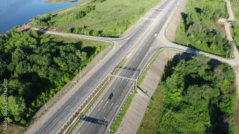 The camera follows the road with passing cars.This is a lake on the left side of the highway.Asphalt road between the trees.Aerial shooting.Birds eye view. The camera follows the road with passing cars.This is a lake on the left side of the highway.Asphalt road between the trees.Aerial shooting.Birds eye view.