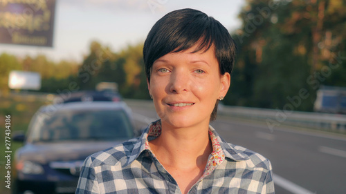 Portrait young brunette beside road. Happy smiling woman with short haircut looking at the camera with friendly smile.