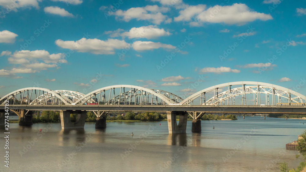 The movement of clouds over the bridge along which cars and trains are moving, a river flows under the bridge, and early autumn has come. pro res 444