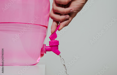 A man pours water from a water dispenser. Concept of lifestyle, drinking water, being thirsty. Filling the glass with a drink, taking care of proper hydration. photo