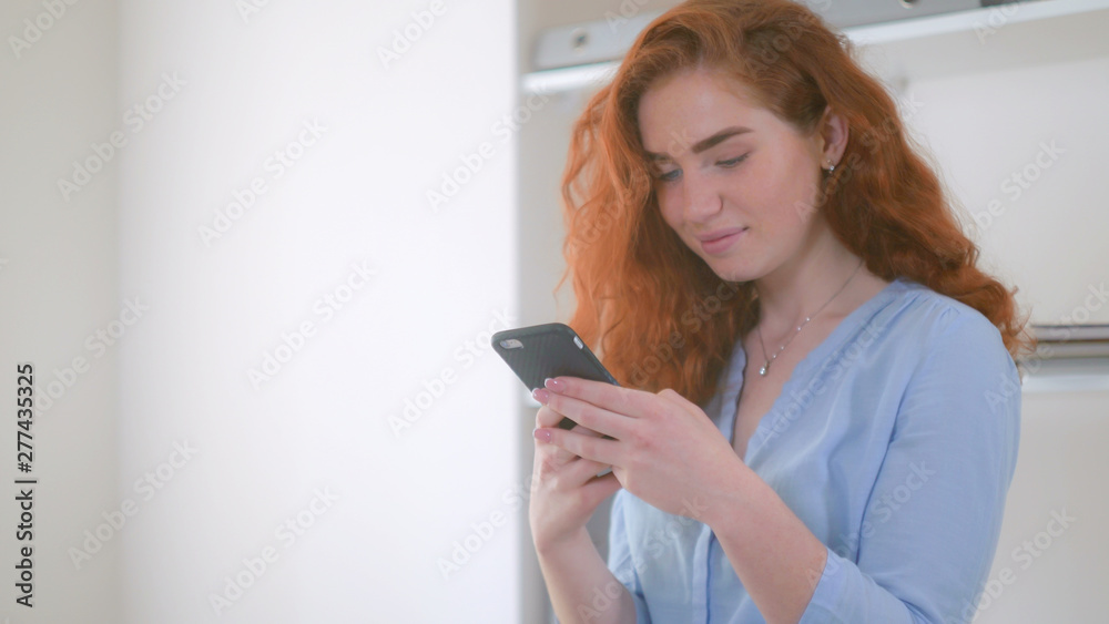 redheaded girl chatting smiling using smartphone. Woman with curly red hair using app on mobile phone for chatting in social net. redheaded girl chatting smiling using smartphone. Woman with curly red hair using app on mobile phone for chatting in social net.