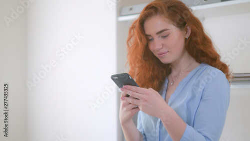 redheaded girl chatting smiling using smartphone. Woman with curly red hair using app on mobile phone for chatting in social net.