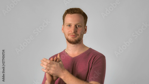 caucasian guy with red hair applauds. handsome redheaded men wearing in casual t-shirt. Portrait ginger young caucasian man clapping hands on grey background photo