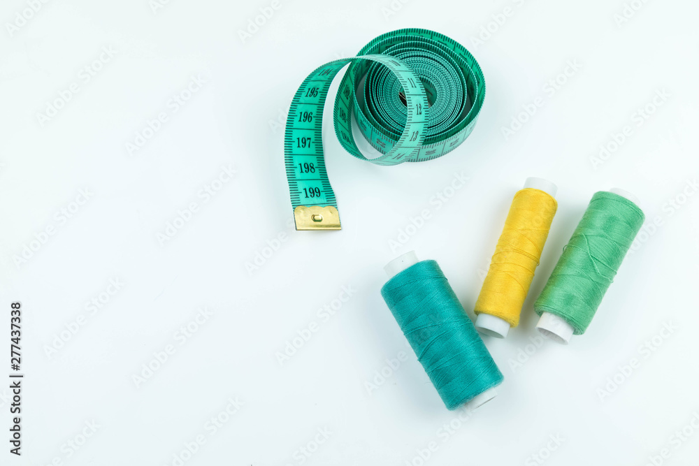 Set of sewing accessories: The green measuring centimetric tape curtailed by a spiral on a white background and coils with strings of yellow and green colors Set of sewing accessories: The green measuring centimetric tape curtailed by a spiral on a white background and coils with strings of yellow and green colors