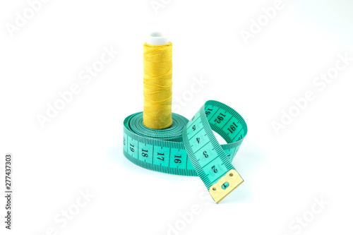 Set of sewing accessories: The green measuring centimetric tape curtailed by a spiral on a white background and the coil with strings of yellow color in the center of a tape photo