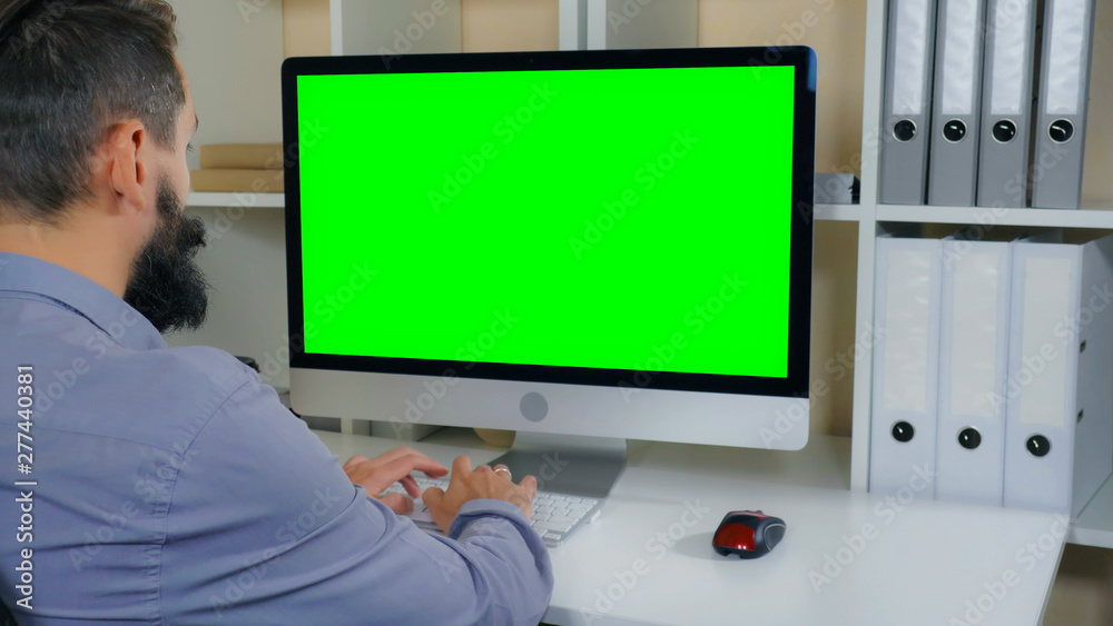 businessman sitting at workplace in small office. man with beard looking on display computer with green screen. employee in startup company typing on keyboard businessman sitting at workplace in small office. man with beard looking on display computer with green screen. employee in startup company typing on keyboard