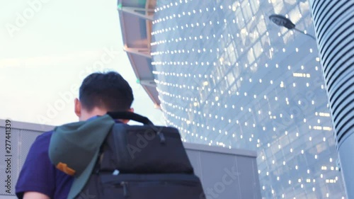 View from the back of man in dark blue t-shirt and with black backpack walking near the large football stadium in summer day. Action. Football fans or sportsmen photo