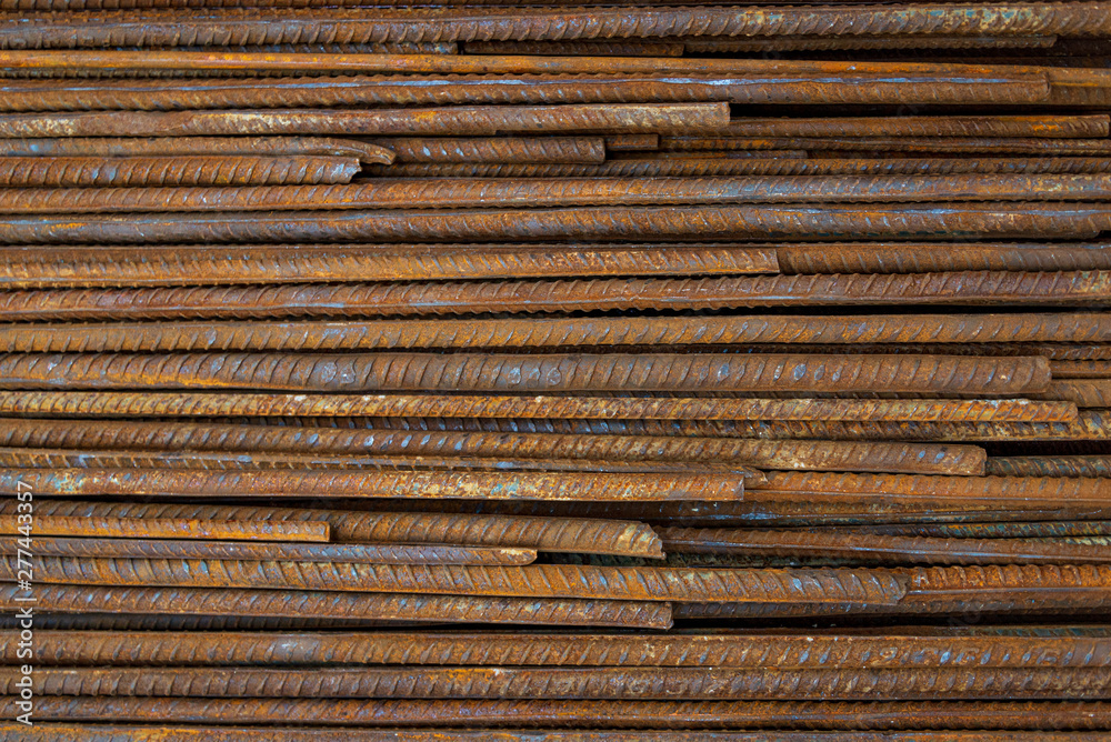 Top view stack of straight old rusty high yield stress deformed reinforcement steel or iron bars. Background horizontal random pattern of deformed iron bars. 