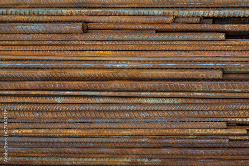 Top view stack of straight old rusty high yield stress deformed reinforcement steel or iron bars. Background horizontal random pattern of deformed iron bars. 