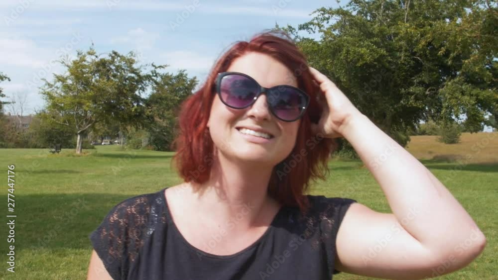 Happy, smiling confident red head woman walking outdoors in nature, green meadow with long grass Happy, smiling confident red head woman walking outdoors in nature, green meadow with long grass