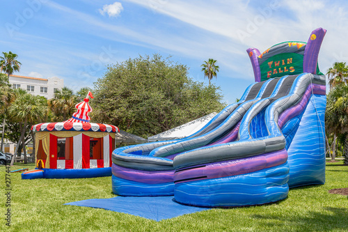 Inflated vintage colorful patriotic small gazebo bounce house sits in the background next the giant inflated twin falls water slide. An open-air park is a perfect spot for community people to enjoy. photo