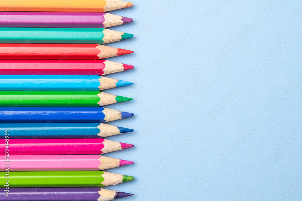 Colorful background with many pencils crayons pastels lined up on multi color backdrop - Top view flat lay