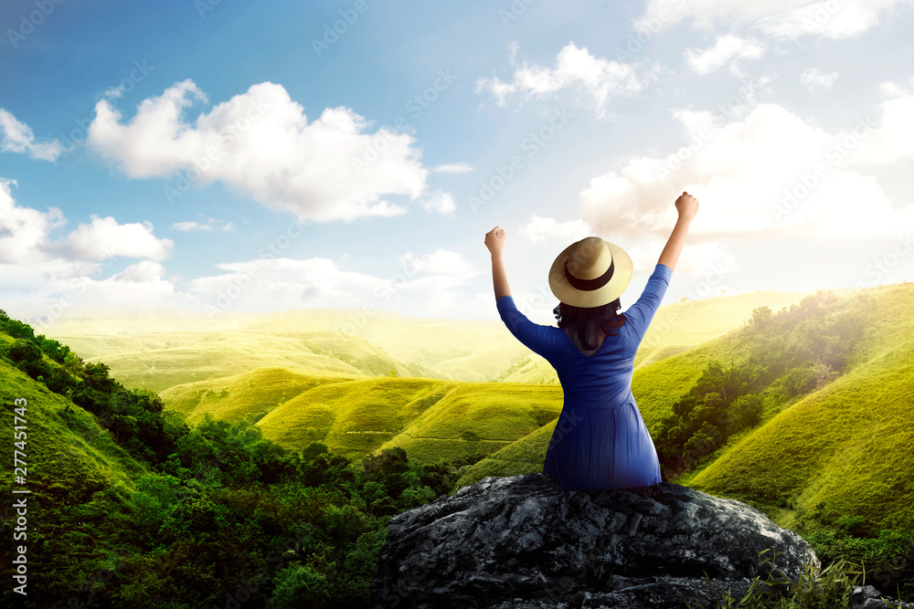 Rear view of asian woman in hat sitting on the rock and looking at green views Rear view of asian woman in hat sitting on the rock and looking at green views