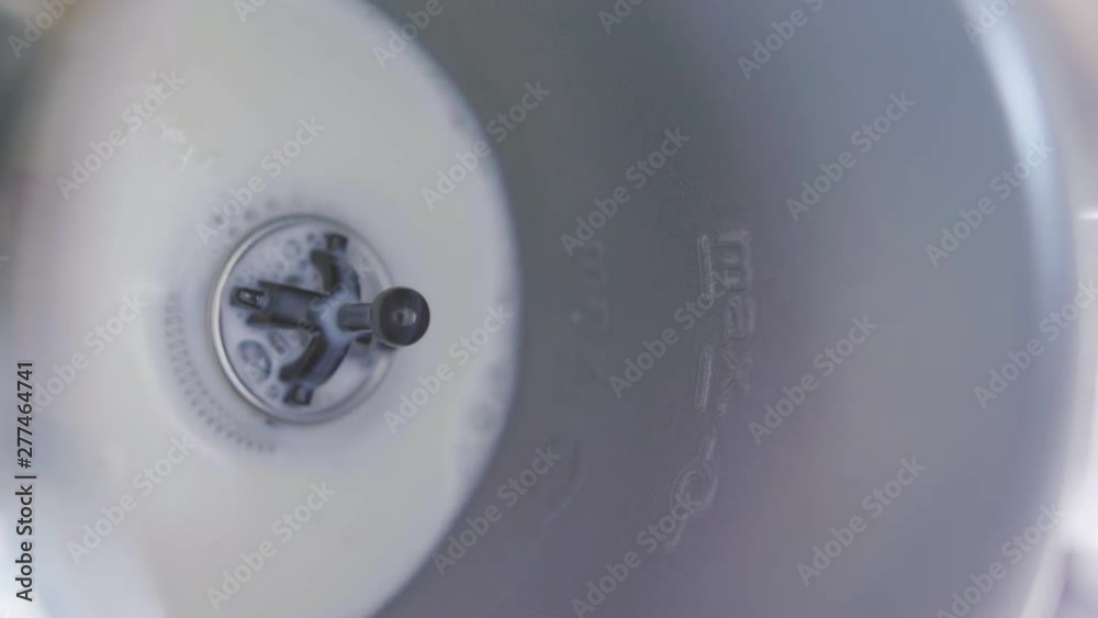 Closeup view of milk being slowly poured into modern compact metallic electric milk frother with small whisk mounted on its bottom. Vertical video frame 9x16.