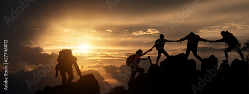 Silhouette of Hikers climbing up mountain cliff. Climbing group helping each other while climbing up in sunset. Concept of help and teamwork, Limits of life and Hiking success full. photo