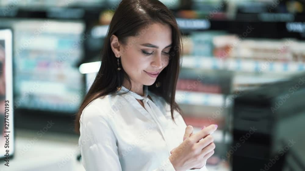 Pretty girl chooses lipstick in cosmetics shop, chooses color, slow motion