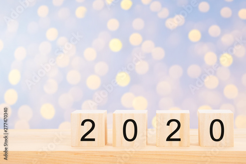 Happy new year 2020 text on wooden cubes on wooden pine table and blur light bokeh background. Banner with copy space for text.