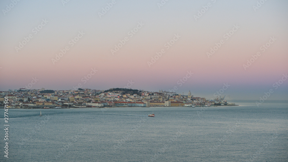 Panorama of Lisbon City, Portugal, taken from Cacilhas across the Tejo River against blue sky after sunset.