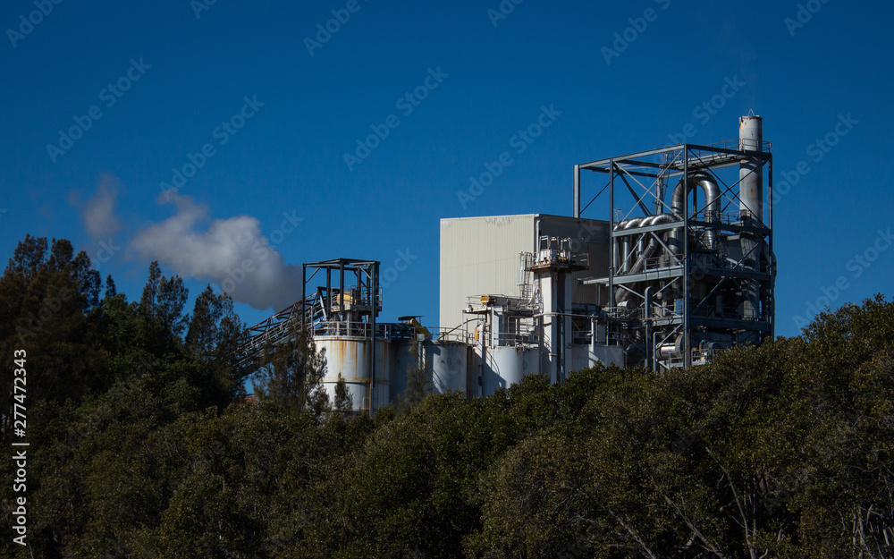 Factory building set on riverbank with steam evaporating to blue sky from chimney Factory building set on riverbank with steam evaporating to blue sky from chimney