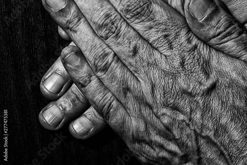 Black and white photo of senior man crossed hands detail on a dark wooden background © Maxal Tamor