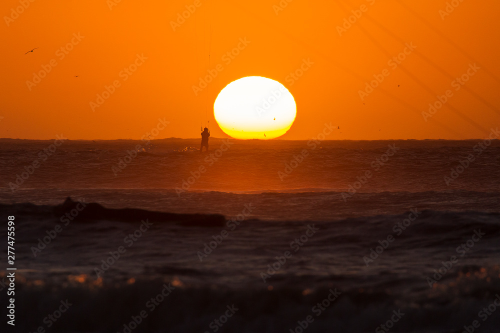 Silhoutte of kitesurfers enjoying big waves at sunset over the sun in Essaouira, Morocco. Beautiful landscape in background Silhoutte of kitesurfers enjoying big waves at sunset over the sun in Essaouira, Morocco. Beautiful landscape in background