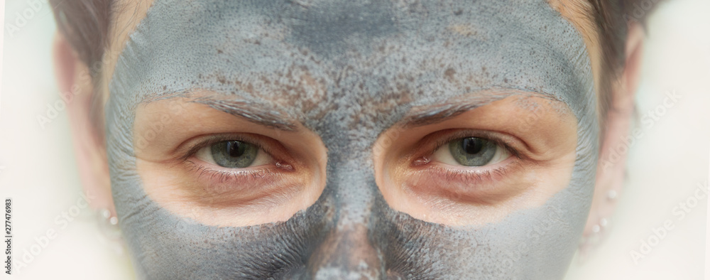 Fototapeta premium Skin care. Woman face with cosmetic spa clay mask closeup. Girl model with grey mask doing beauty spa treatment