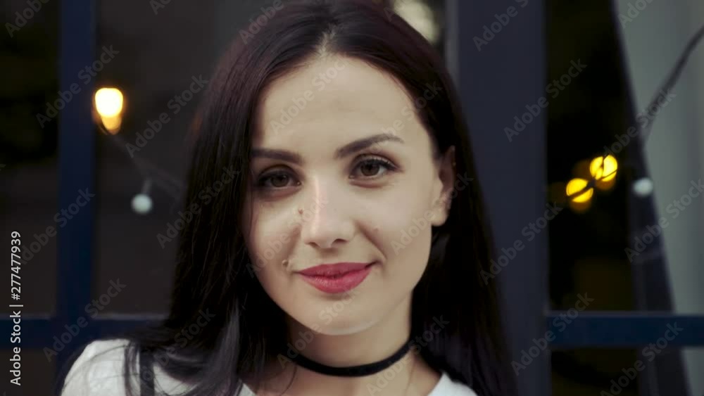 Portrait of a girl. A young woman with black hair and moles on her face looks into the camera against the backdrop of the backlight in the cafe window. Portrait of a girl. A young woman with black hair and moles on her face looks into the camera against the backdrop of the backlight in the cafe window.