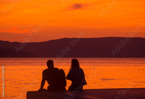a girl and a guy on the pier watching at sunset at the sea