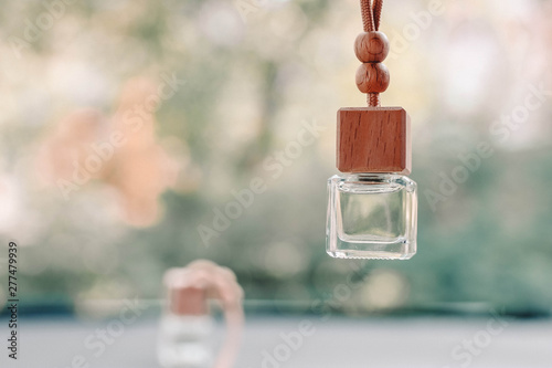 Small glass bottle with car perfume hanging in the car. Beautiful blurred background outside the window.