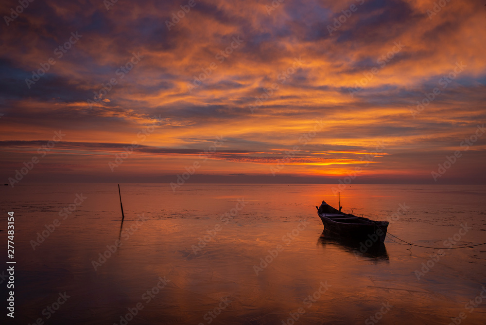 Naklejka premium Colorful sunrise at sea, with a boat floating on the clam water and clouds reflecting on the water