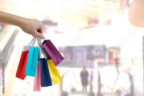 Crop female hand holding colorful paper bags on background of shopping center.