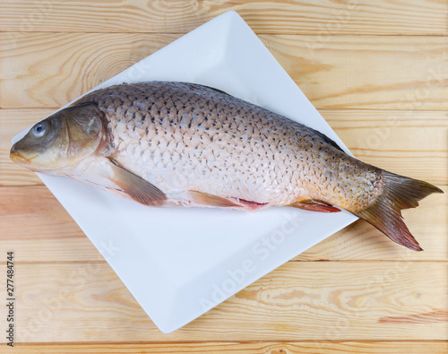 Raw carp prepared for cooking on dish on wooden surface