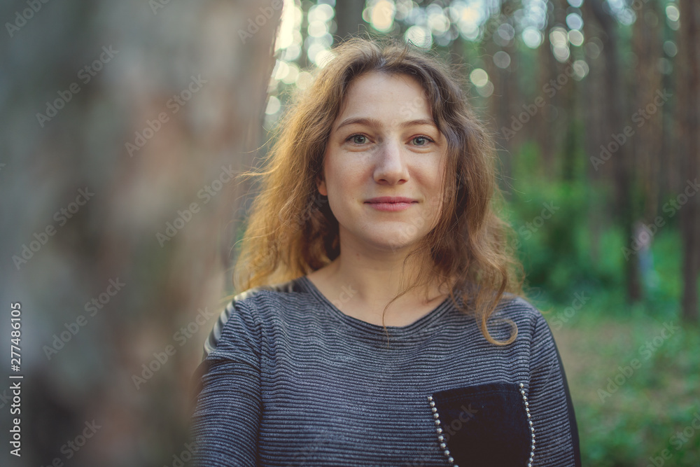 Serious woman looking out from behind tree. Pretty calm woman touching tree and looking at camera in quiet forest Serious woman looking out from behind tree. Pretty calm woman touching tree and looking at camera in quiet forest