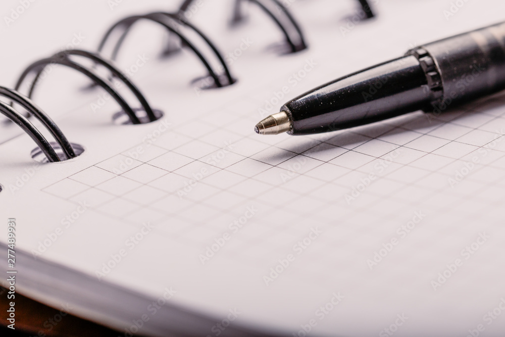 Opened notepad in a cage with an automatic plastic ballpoint pen close-up. toned Opened notepad in a cage with an automatic plastic ballpoint pen close-up. toned
