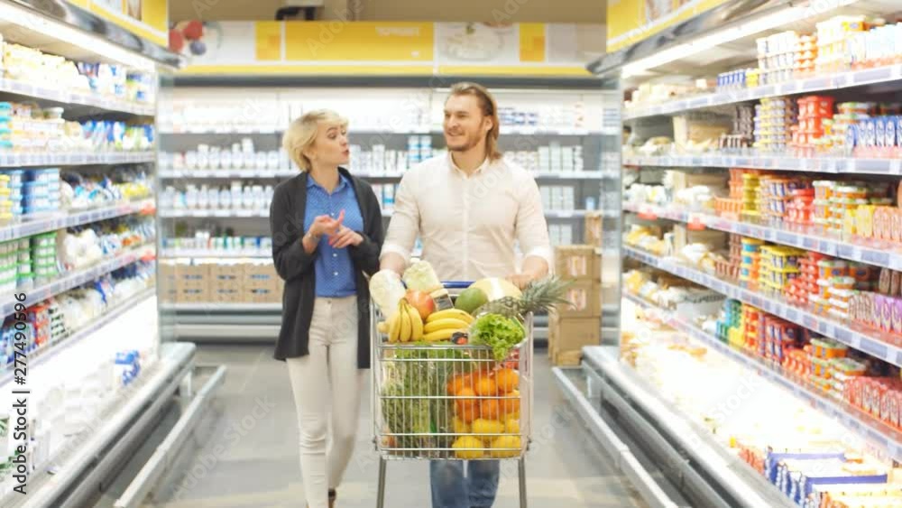 Positive family customers with full trolley of healthy organic vegetables and fruits in grocery store during weekly food shopping