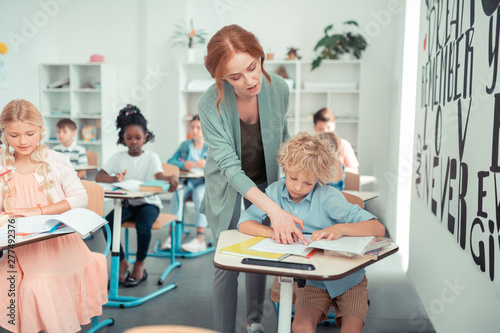 Teacher helping a schoolboy to read the task.