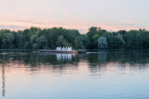 Water landscape at sunset with a fountain located in the middle of the lake.