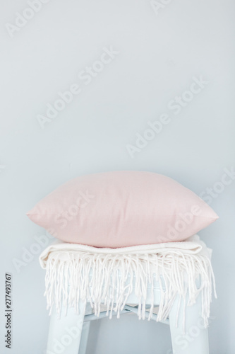Minimalistic skandinavian picture of a light pink pillow and a white plaid on the chair near a pale blue wall photo
