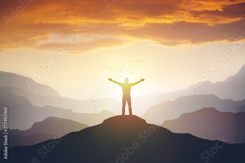 Climber arms up outstretched on mountain top looking at inspirational landscape.