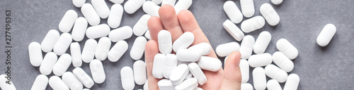 Banner of hand palm of a child with handful of large white tablets with more scattered around, drugs food supplements and medicine safety and consumption concept or immunization with copy space photo