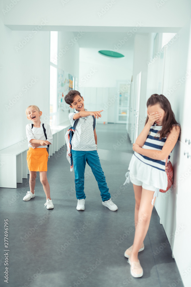 Naklejka premium Rude violent girl and boy laughing at poor dark-haired girl