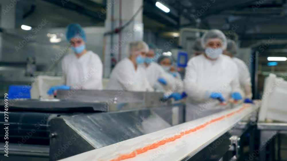 People work at a food factory, taking products from a conveyor.