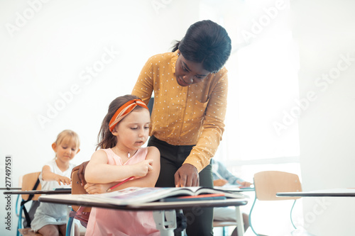 African-American teacher helping cute little girl sitting at the desk