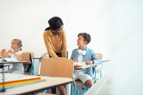 Dark-haired boy smiling while talking to his teacher photo