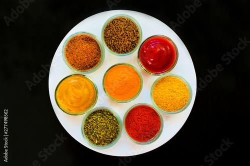 Set of spices and herbs on a white plate. Indian cuisine Pepper, salt, paprika, curry, basil, mustard, nutmeg, turmeric. View from above. Close-up.