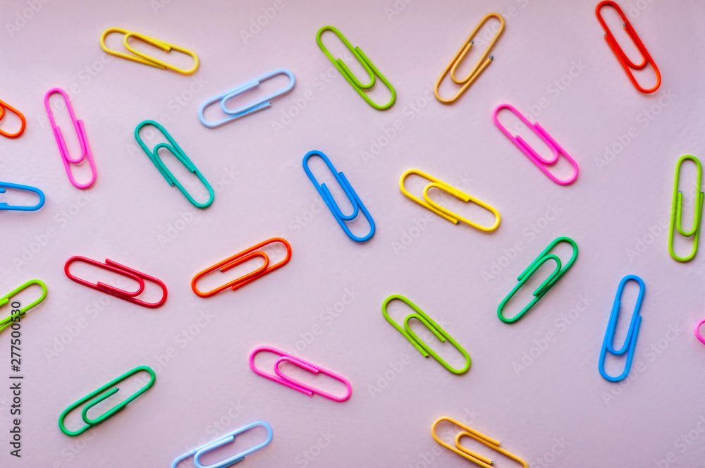 Bright colourful paper clips laying in disorger on a pink background Bright colourful paper clips laying in disorger on a pink background